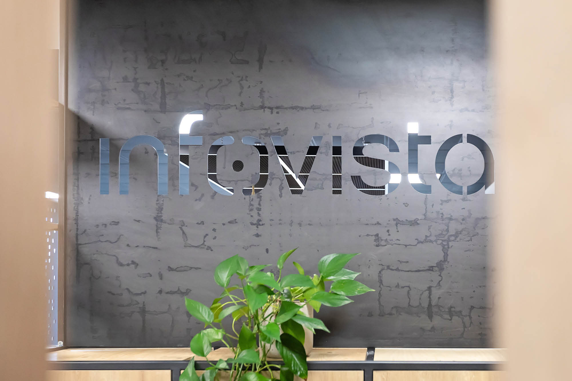 A frosted glass wall with the word infovista partially visible, surrounded by a modern interior. A green plant is in the foreground.