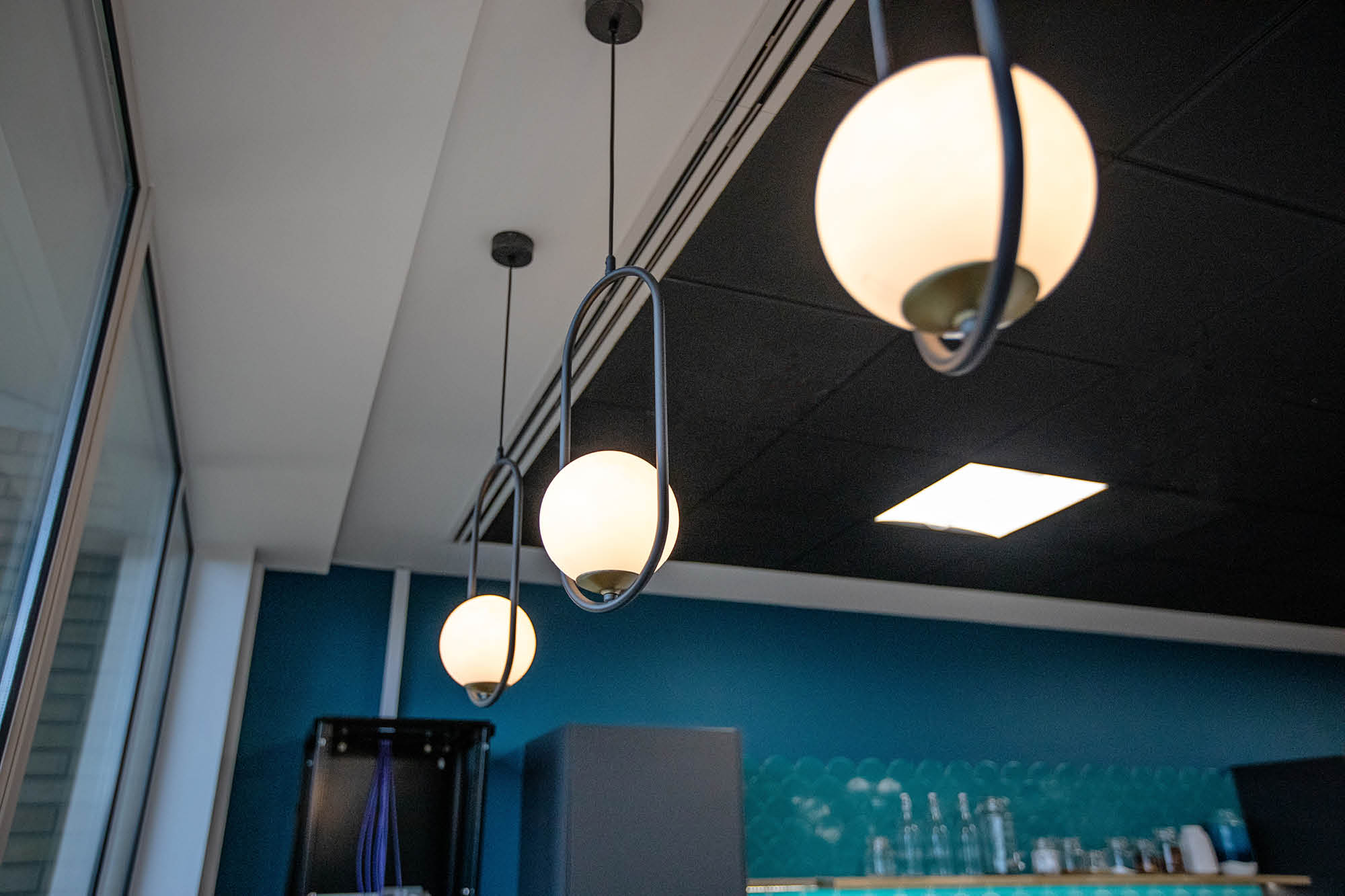 Three modern pendant lights with white spherical shades hanging from a ceiling in a room with blue walls and a black ceiling.