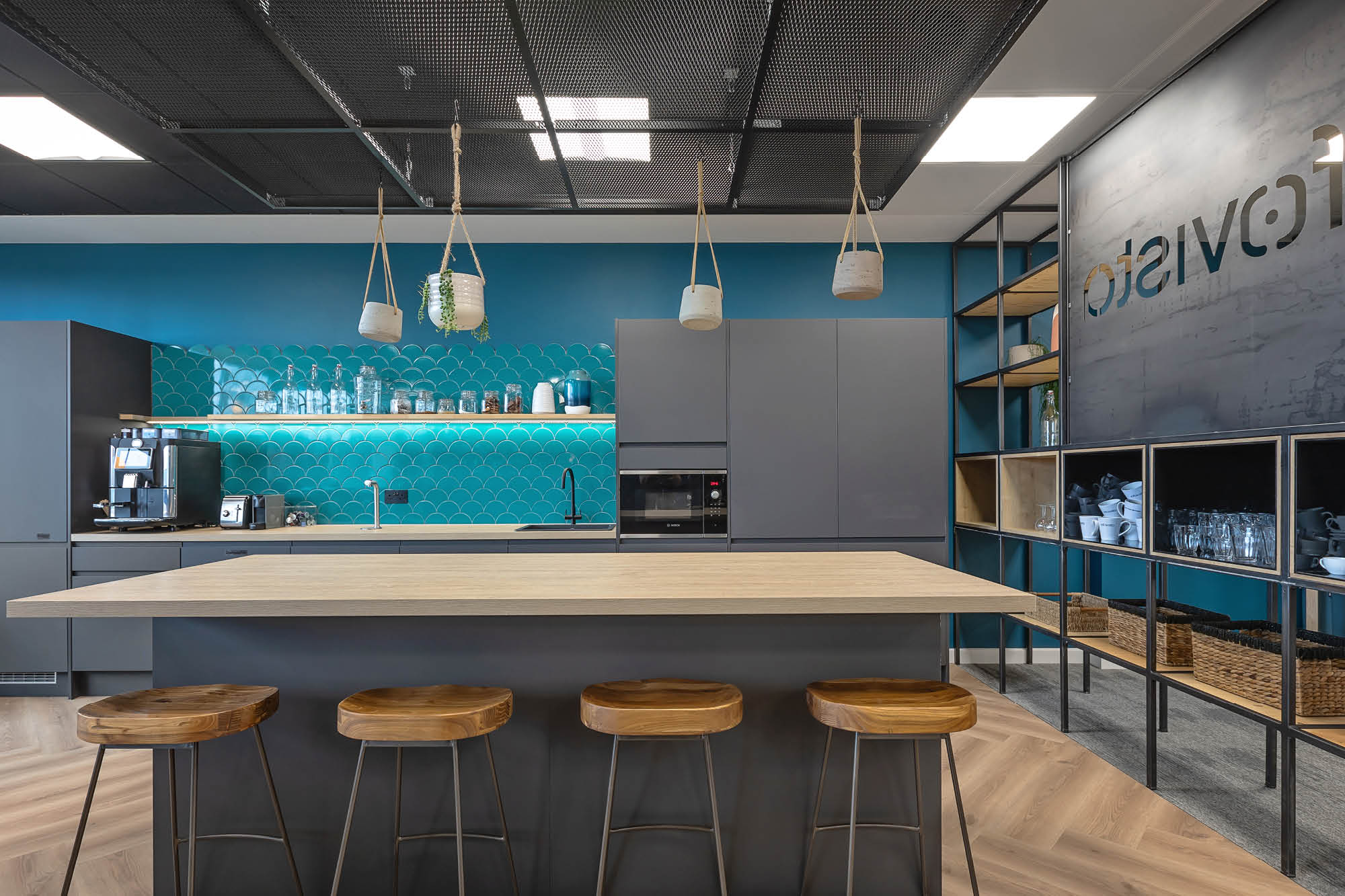 Modern kitchen with a dark teal backsplash and gray cabinets. A wooden island features four stools.