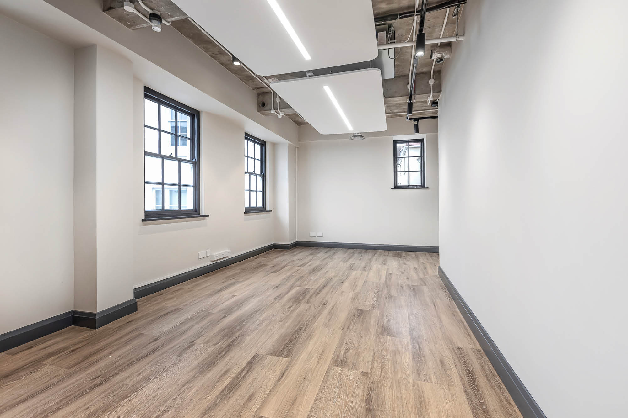 Empty room with light wood flooring, white walls, and large windows letting in natural light.