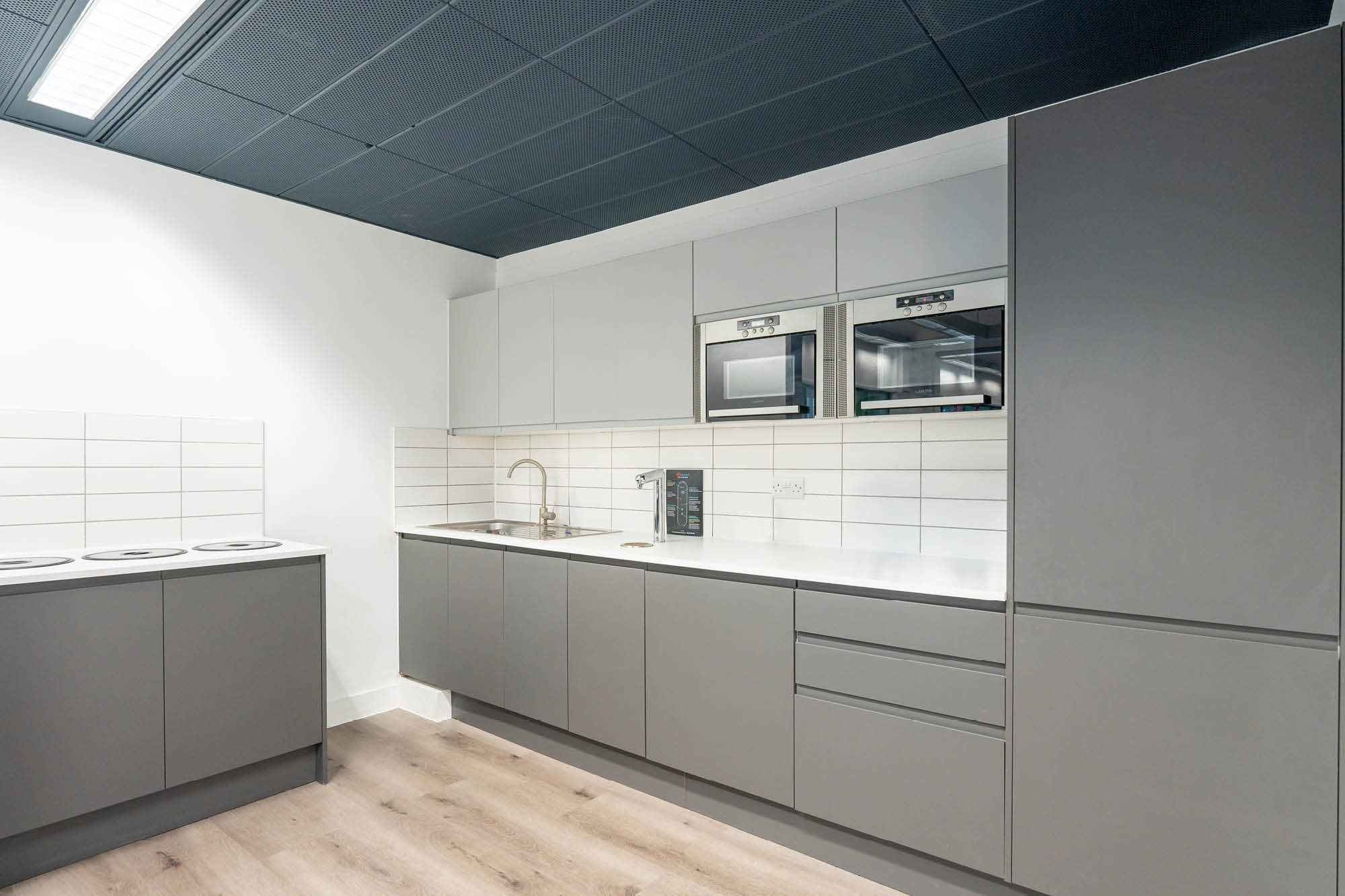 Modern kitchen with grey cabinets, a white countertop, and a tiled backsplash. Includes an oven, microwave, and a sink with a faucet.