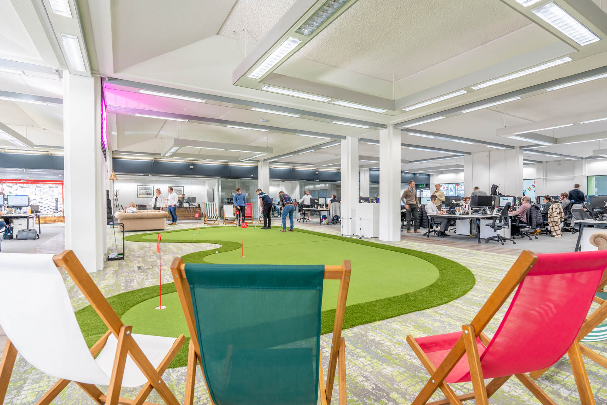 Open office space with a mini golf area in the center, surrounded by people working at desks.