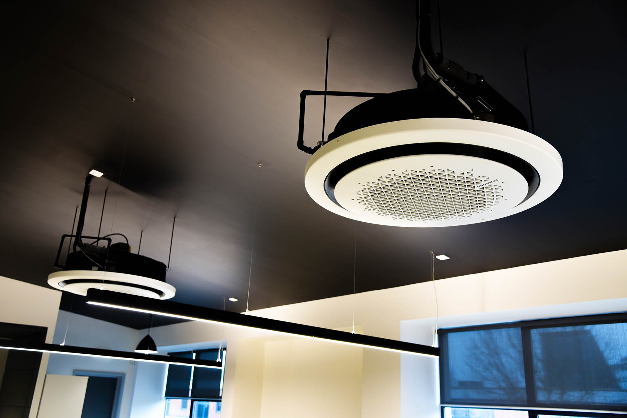 Ceiling-mounted circular air purifiers with black and white design are suspended in a modern room with a dark ceiling.