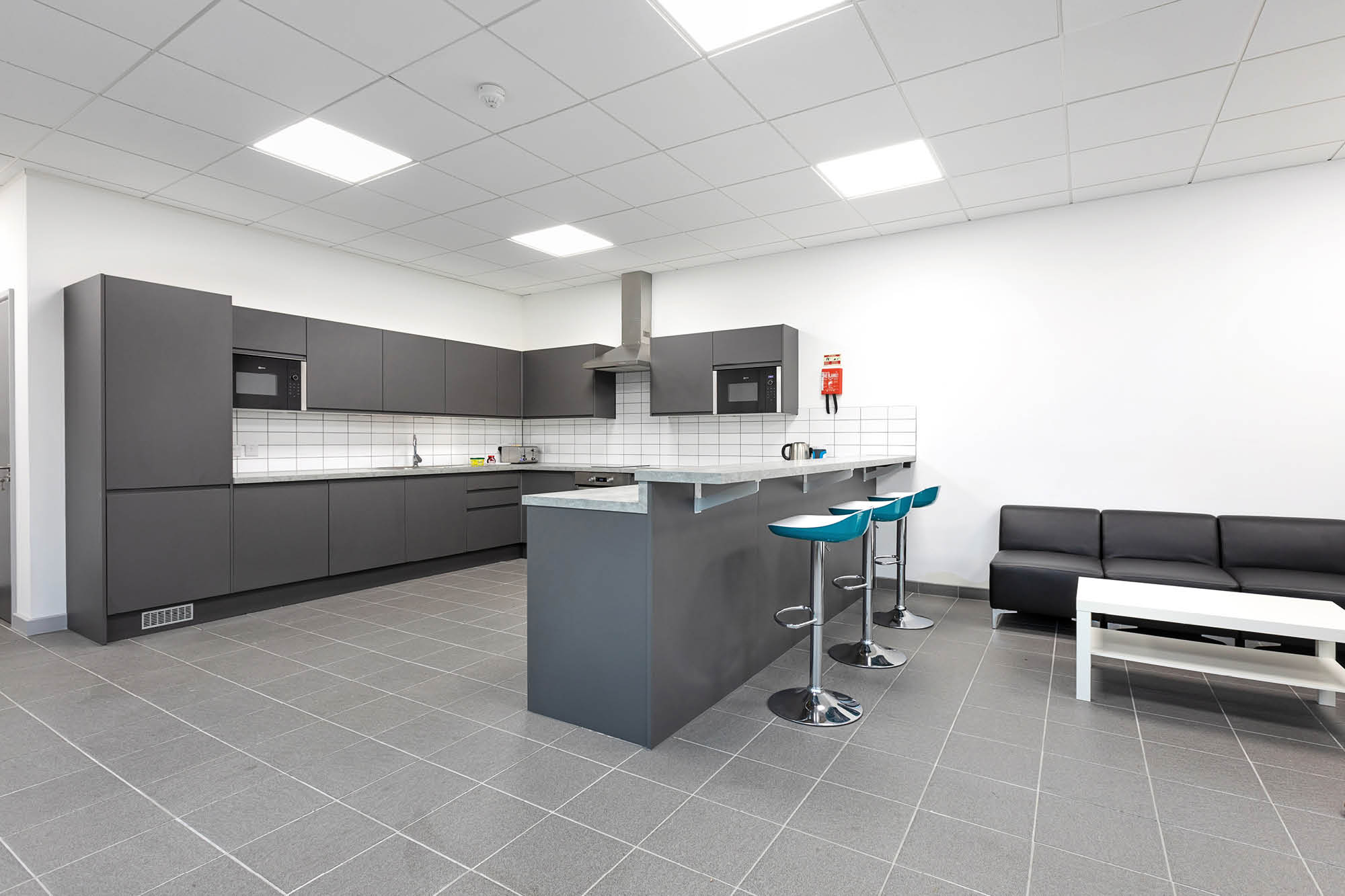 Modern kitchen with gray cabinets, tiled backsplash, and stainless steel appliances. Includes a peninsula with two blue bar stools.