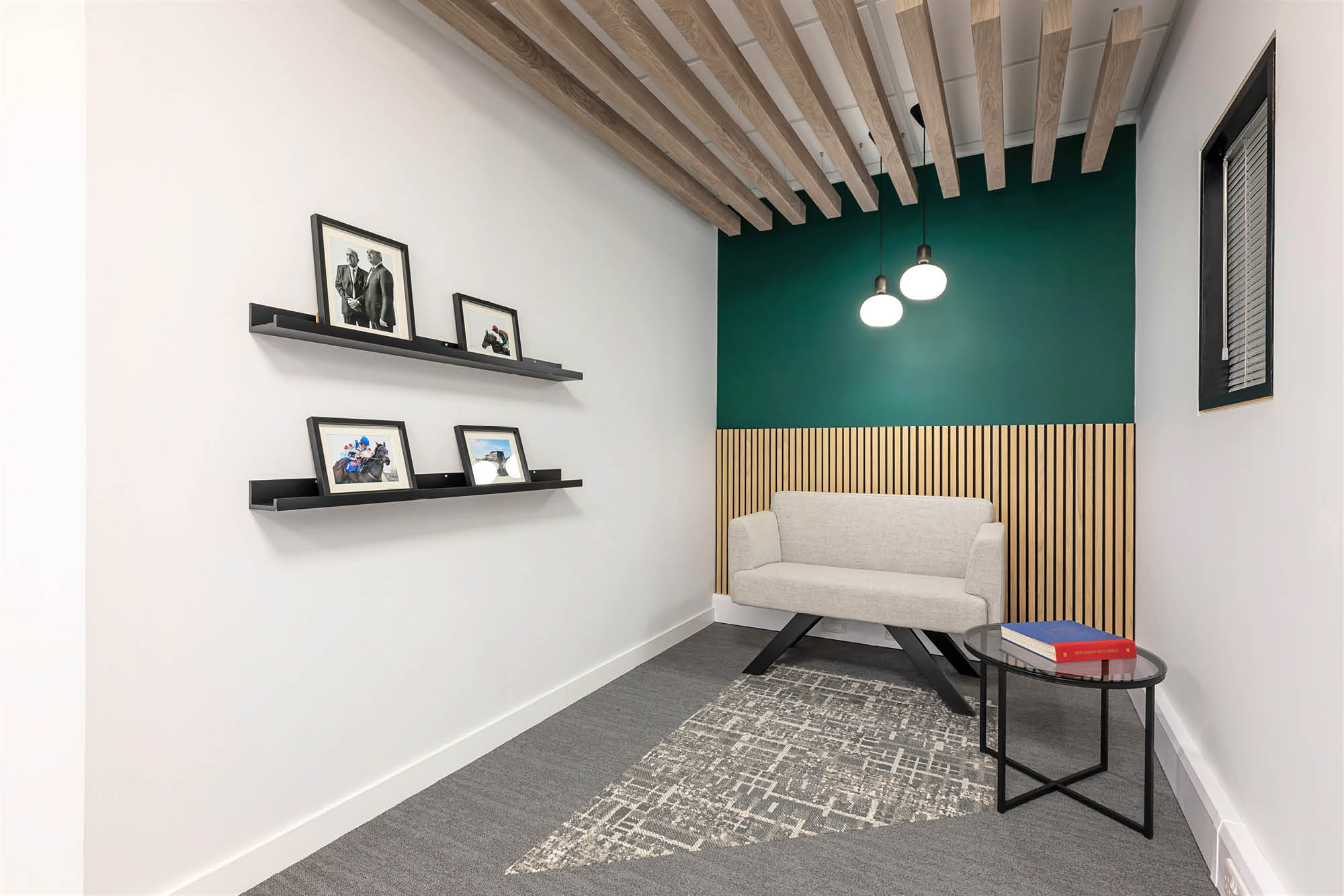 A modern, small room with a gray cushioned bench, green and wood accented walls. Two shelves display framed photos.