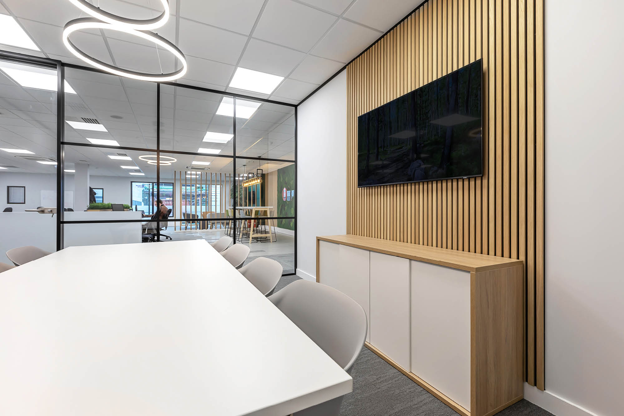 Modern office space with a conference table and chairs. A flat-screen TV mounted on a wood-panelled accent wall.