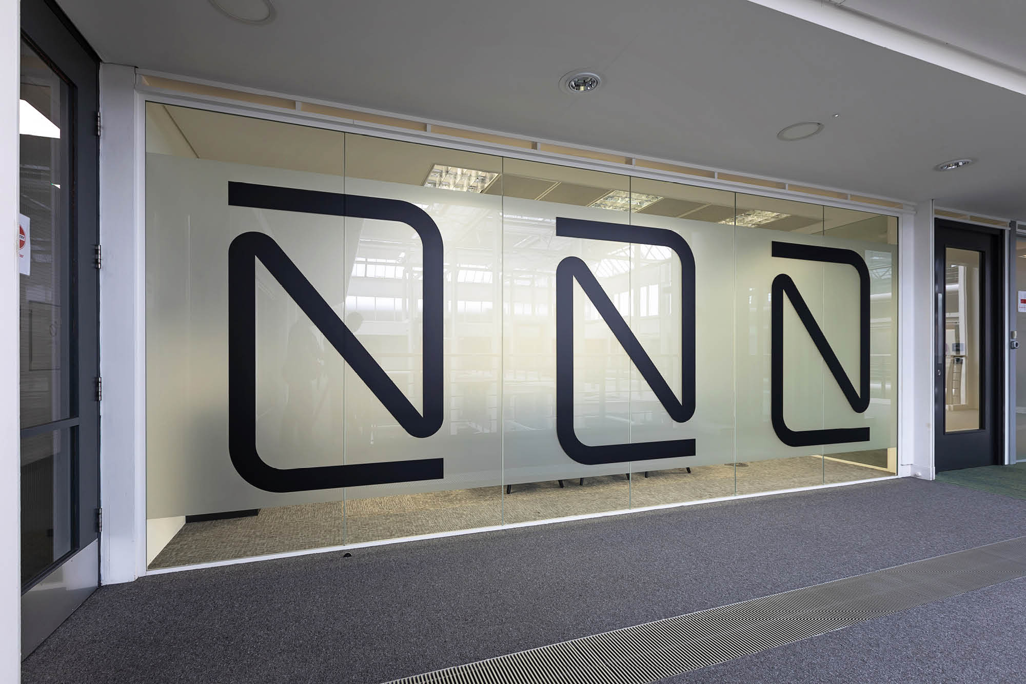 Glass wall with large black geometric N shapes repeats the pattern. Lighting from above reflects off the frosted surface.