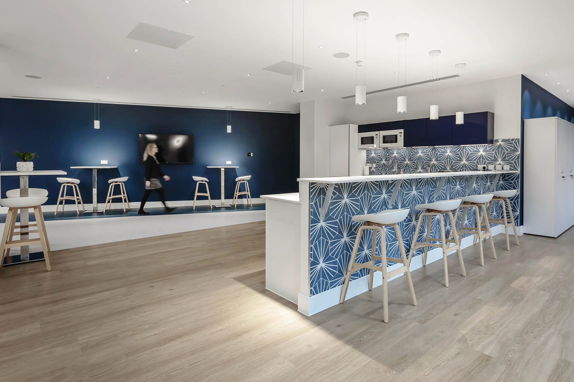 A modern kitchen and lounge area with a wooden floor. The room features a bar counter with a blue patterned front.