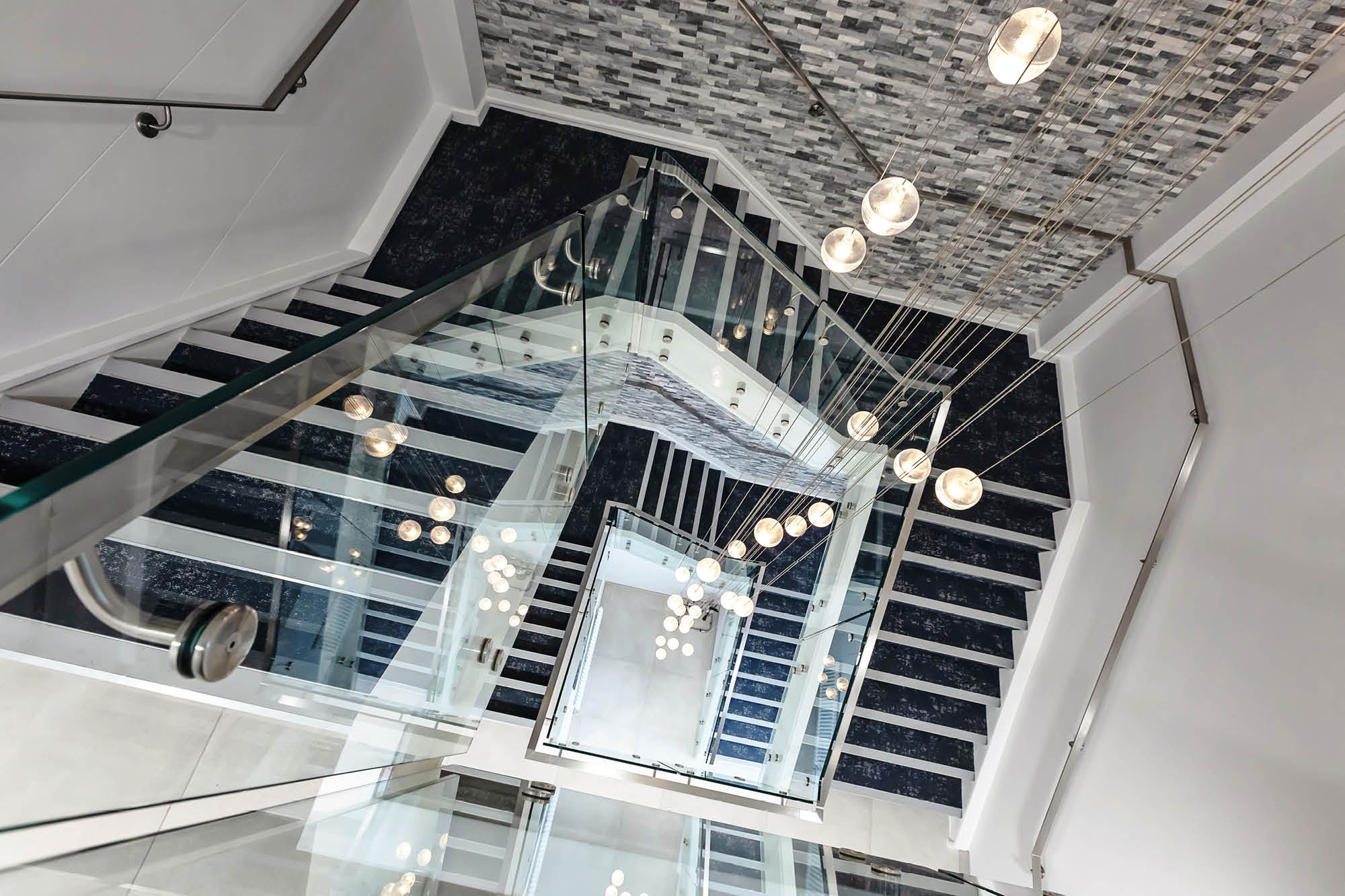 View from the top of a modern staircase with glass railings, looking down multiple flights.