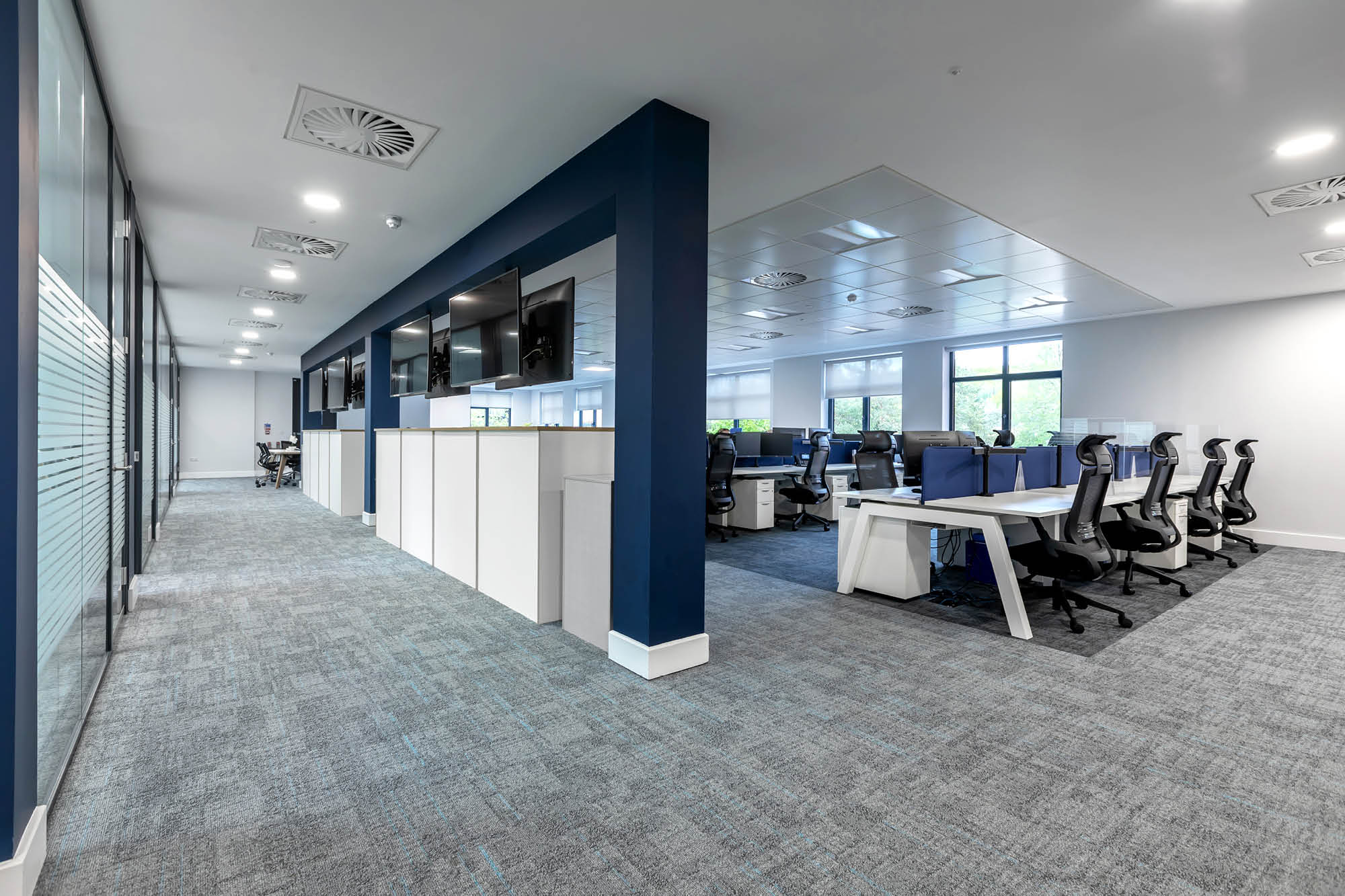 Modern office space with glass partitions, navy blue and white walls, open workstations, and ergonomic chairs.
