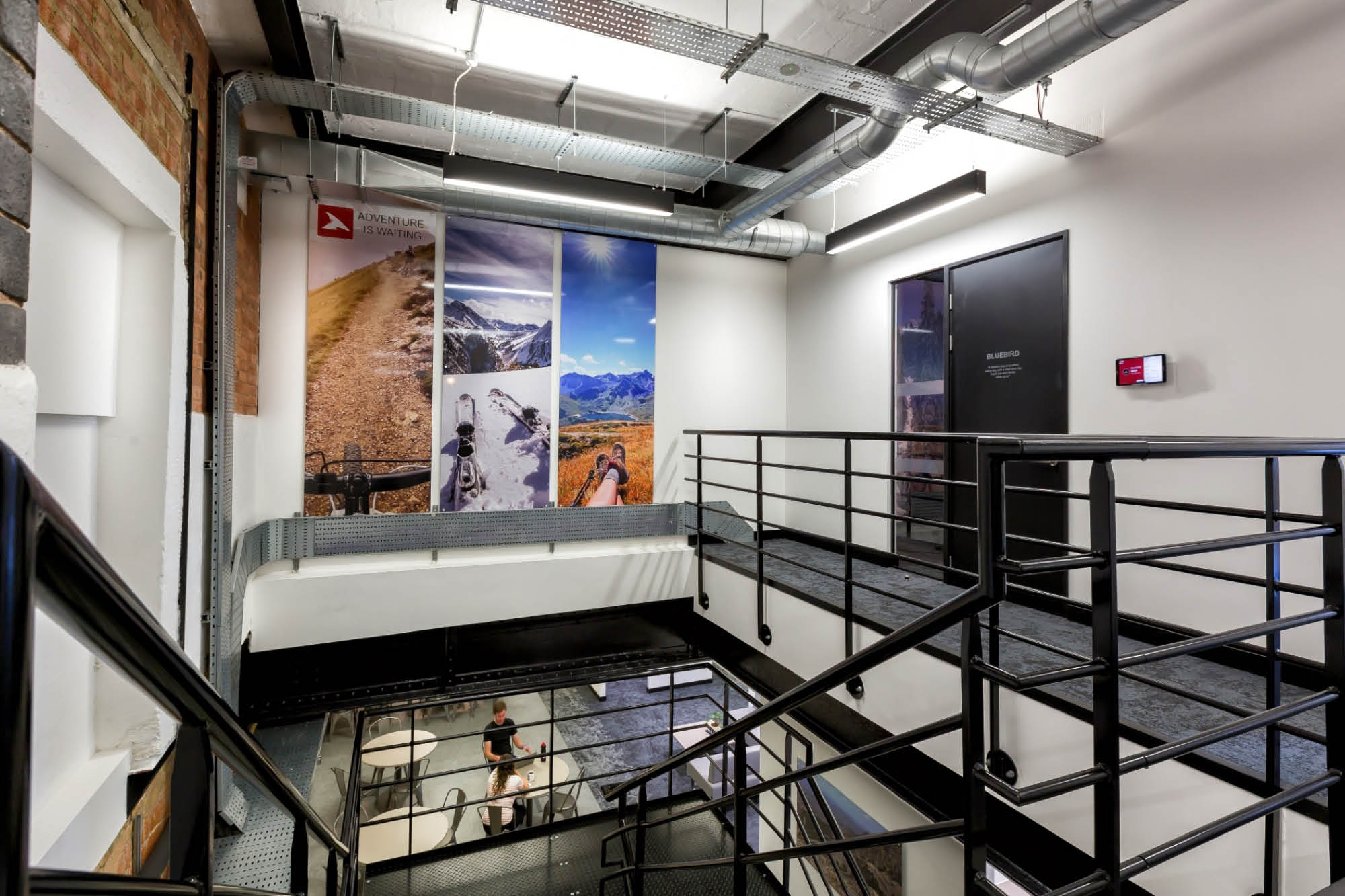 Industrial-style staircase with metal railings and exposed ducts, leading to an upper level. Walls are adorned with mountain landscape photos.