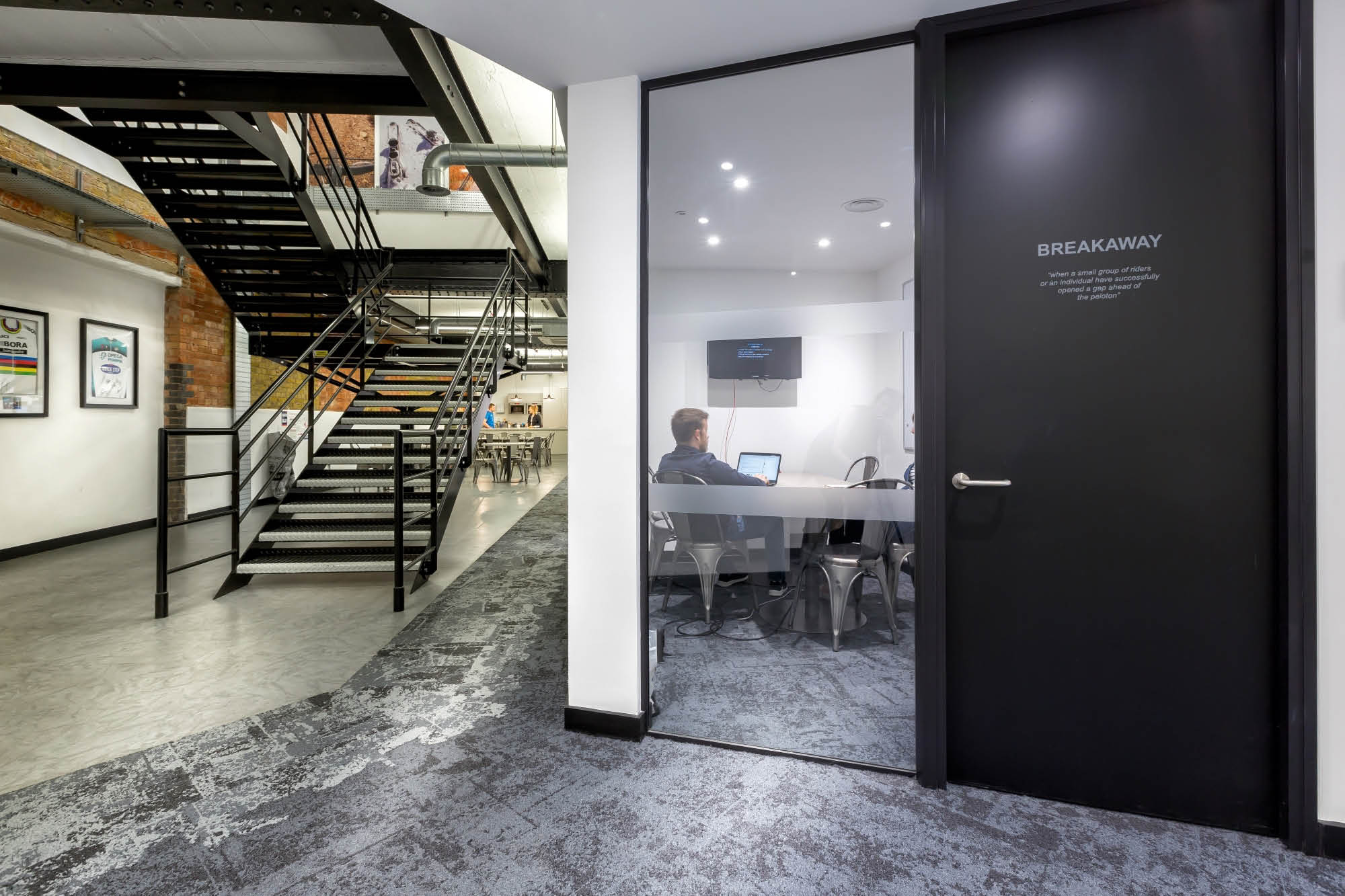 A modern office interior featuring a staircase with metal railing on the left. On the right, a glass-walled meeting room labeled Breakaway.