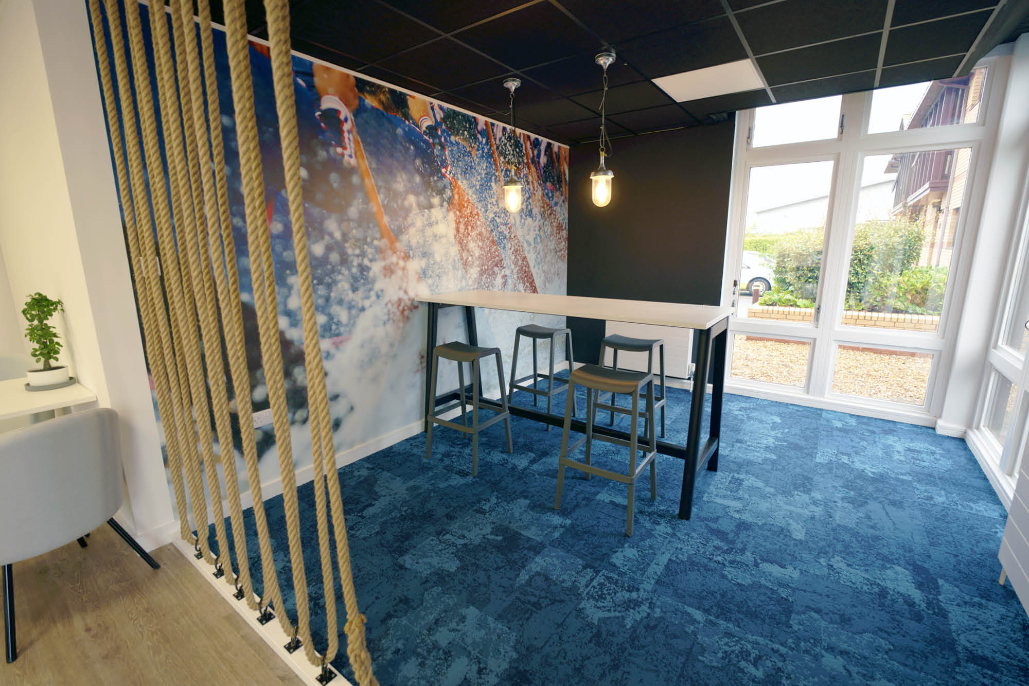Modern office space featuring a high table with stools, rope partition on the left, and a vibrant wall mural.