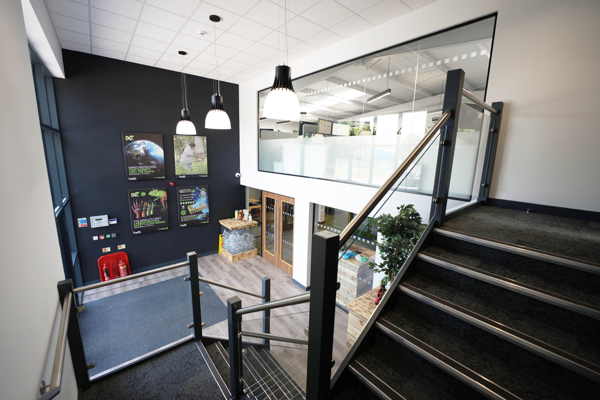 A modern, well-lit interior with a staircase leading to an upper floor. Glass railings and large windows enhance the space.