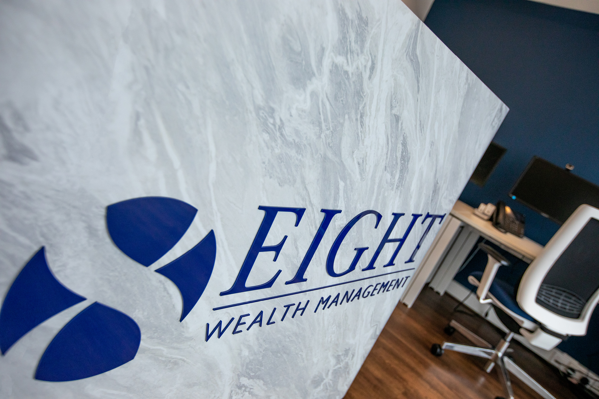 Reception desk with a sign that reads Eight Wealth Management in blue letters against a marbled background.