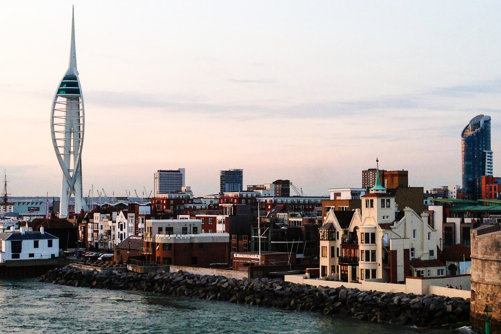 A waterfront cityscape featuring a modern, sail-shaped tower, surrounded by contemporary buildings.