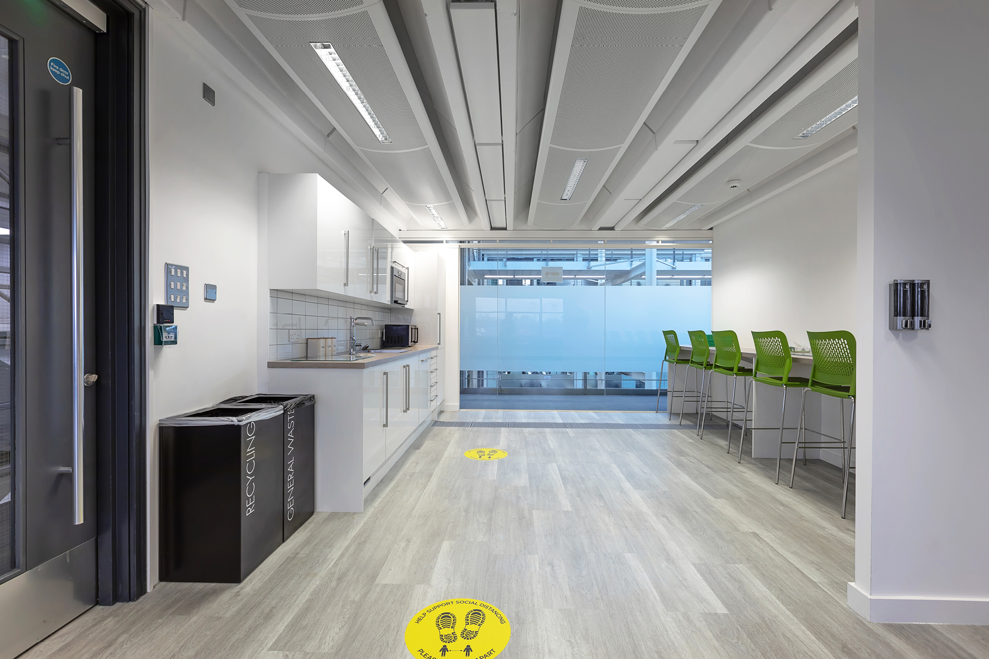 Modern office break room with a kitchenette on the left featuring a sink, microwave, and cabinets.