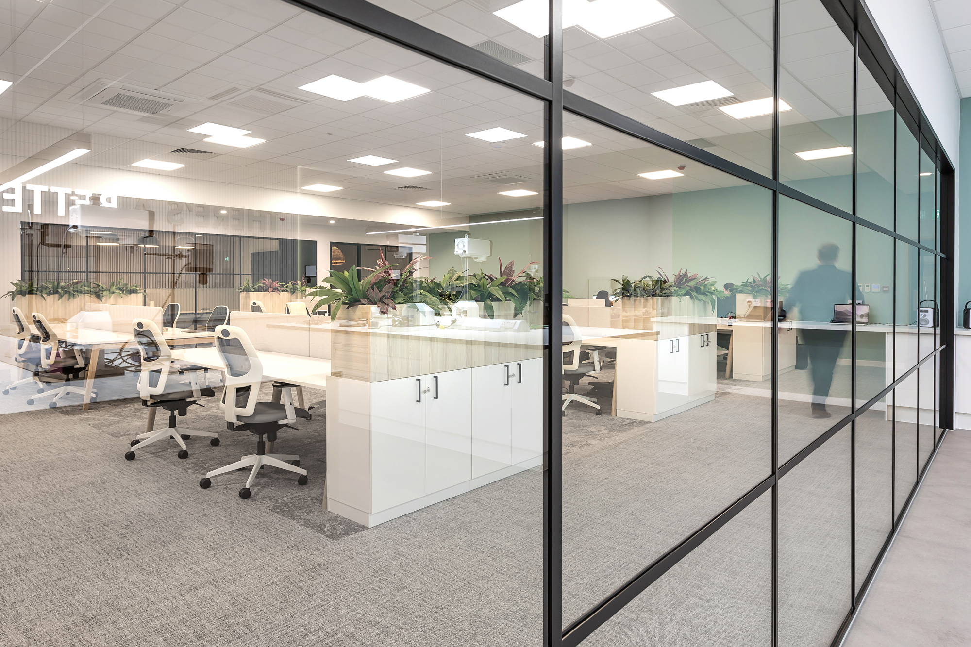 A modern office space with glass walls, featuring white desks and ergonomic chairs.