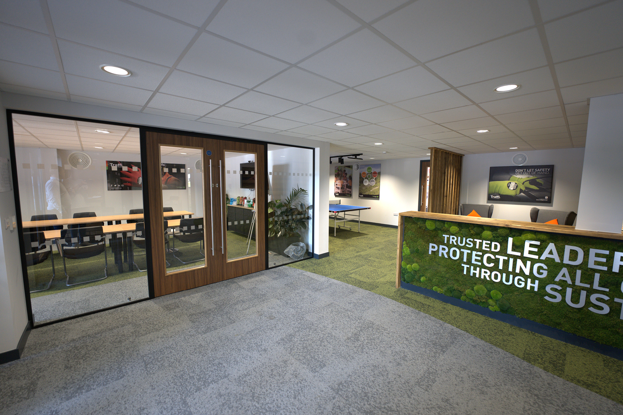 Office with a glass-walled conference room on the left, a reception desk with sustainability message
