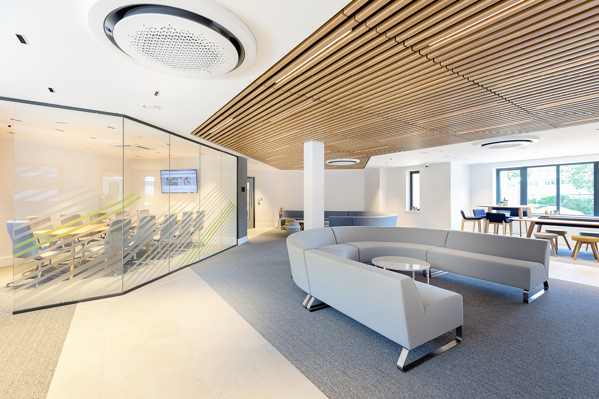 Modern office space with a glass-walled conference room on the left, featuring a long table.