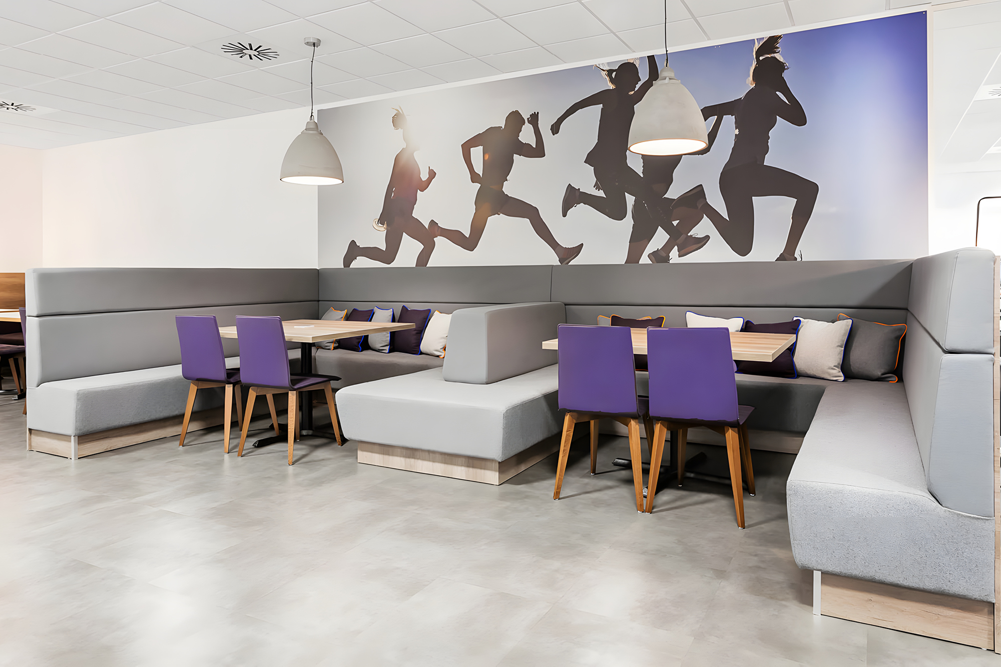 Modern cafe interior with grey upholstered booths and wooden tables, complemented by purple chairs. 