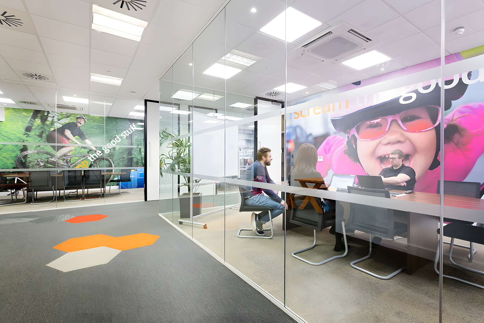 Modern office space with glass-walled meeting room. Two people are seated at a conference table.