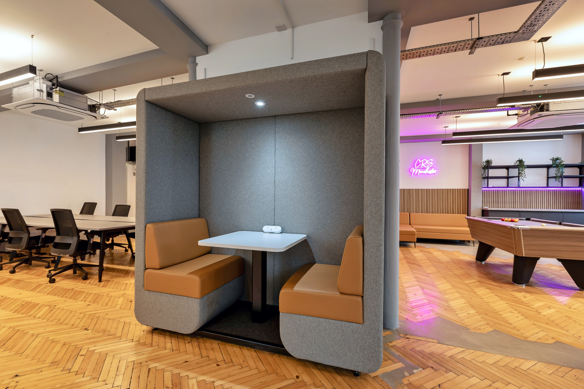 A modern office space featuring a cozy booth with a table and brown cushioned seats.