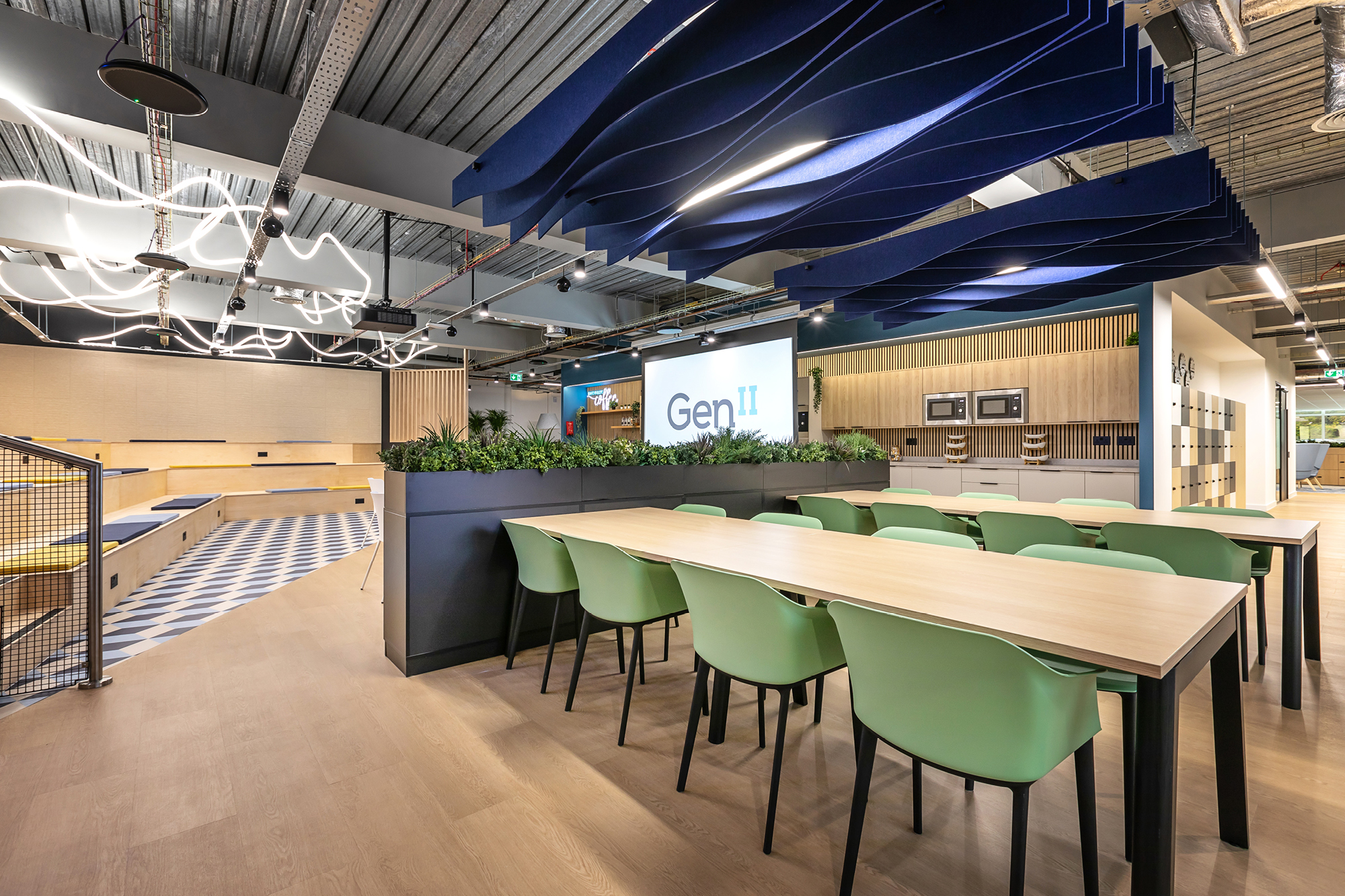 Modern office space with green chairs around wooden tables. Ceiling has blue wave-like panels.