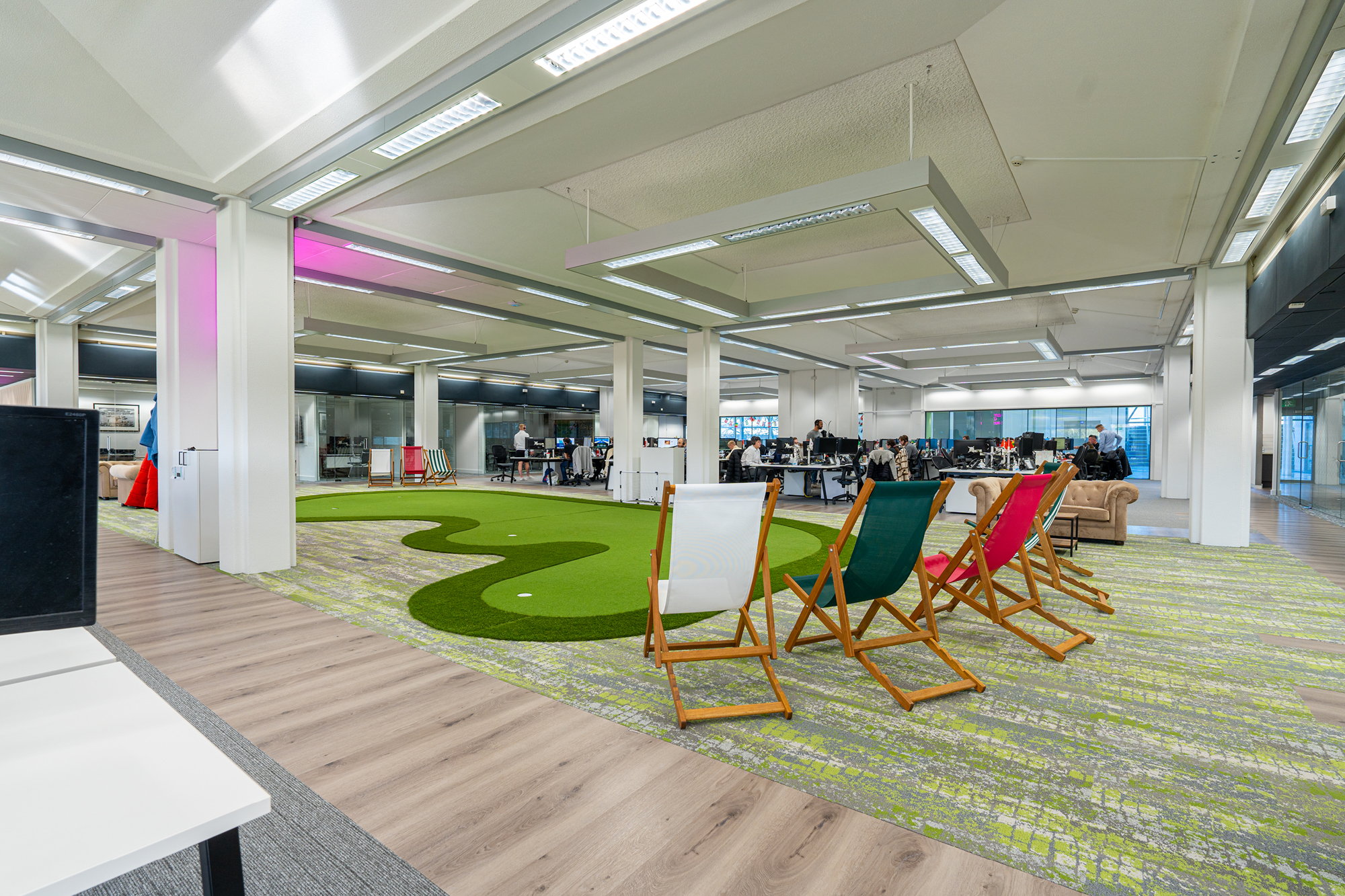 An open office space with a green carpet resembling a putting green. Deck chairs and a sofa.
