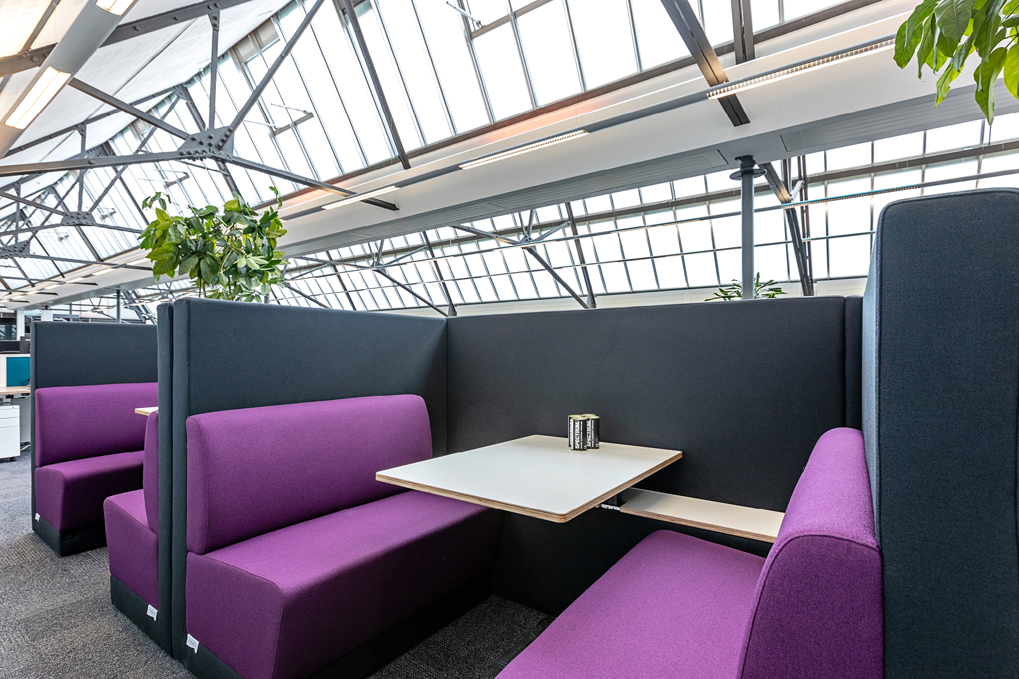 A modern office space features a seating area with two high-backed sofas facing each other, separated by a central partition.
