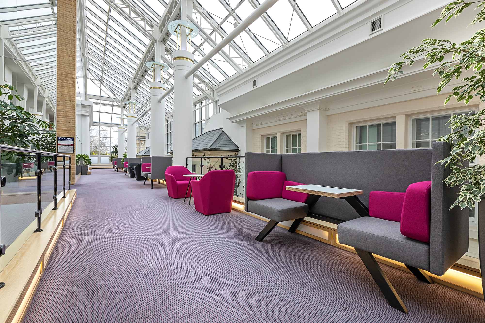 A modern indoor space with a glass ceiling features purple and gray seating areas. There are angular booths with tables.