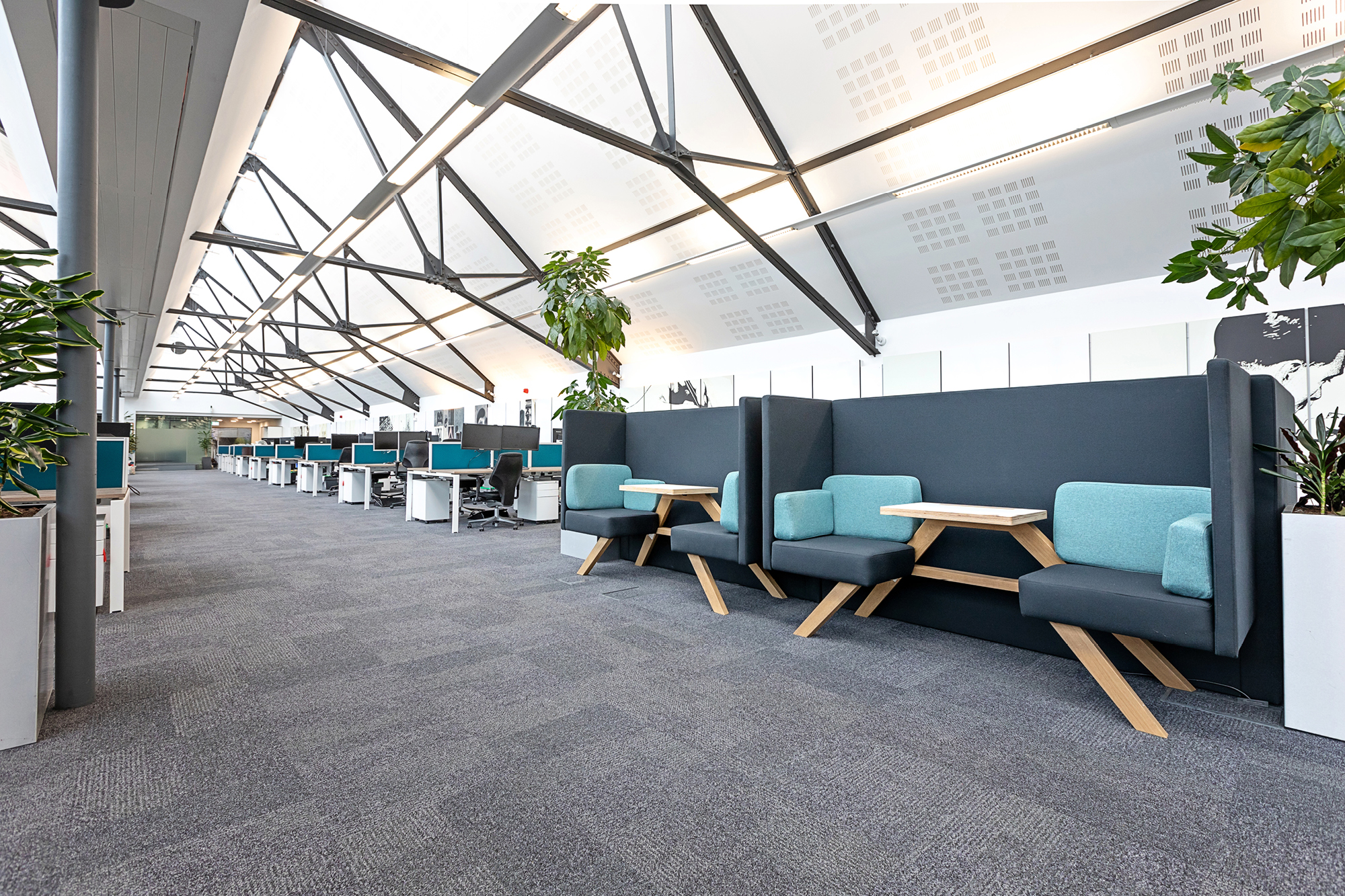 Open-plan office with vaulted ceilings and large windows. Features blue and black seating booths with small wooden tables along a wall.