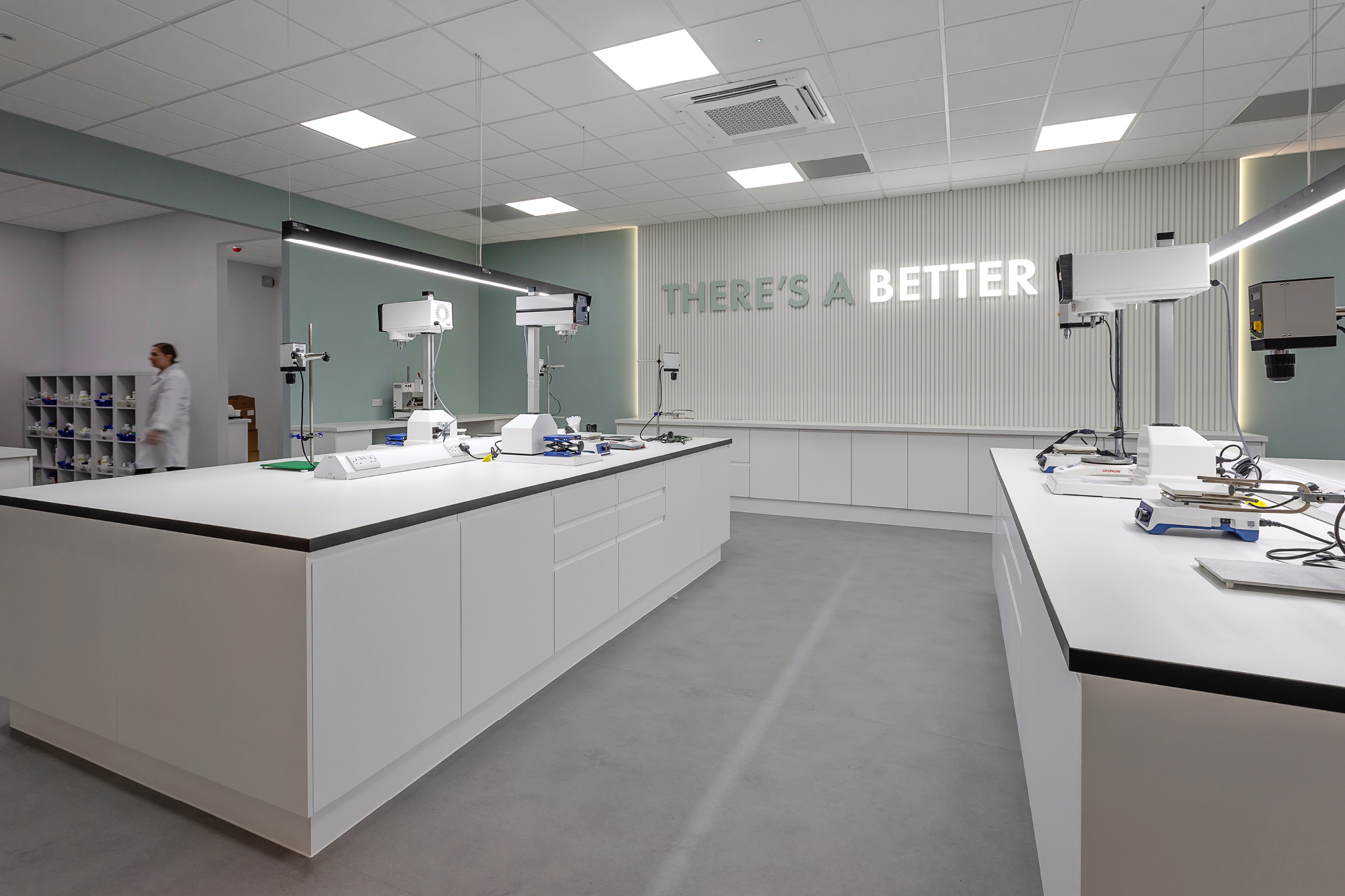 Laboratory space with medical and laboratory equipment setup, white desking and woman in background.