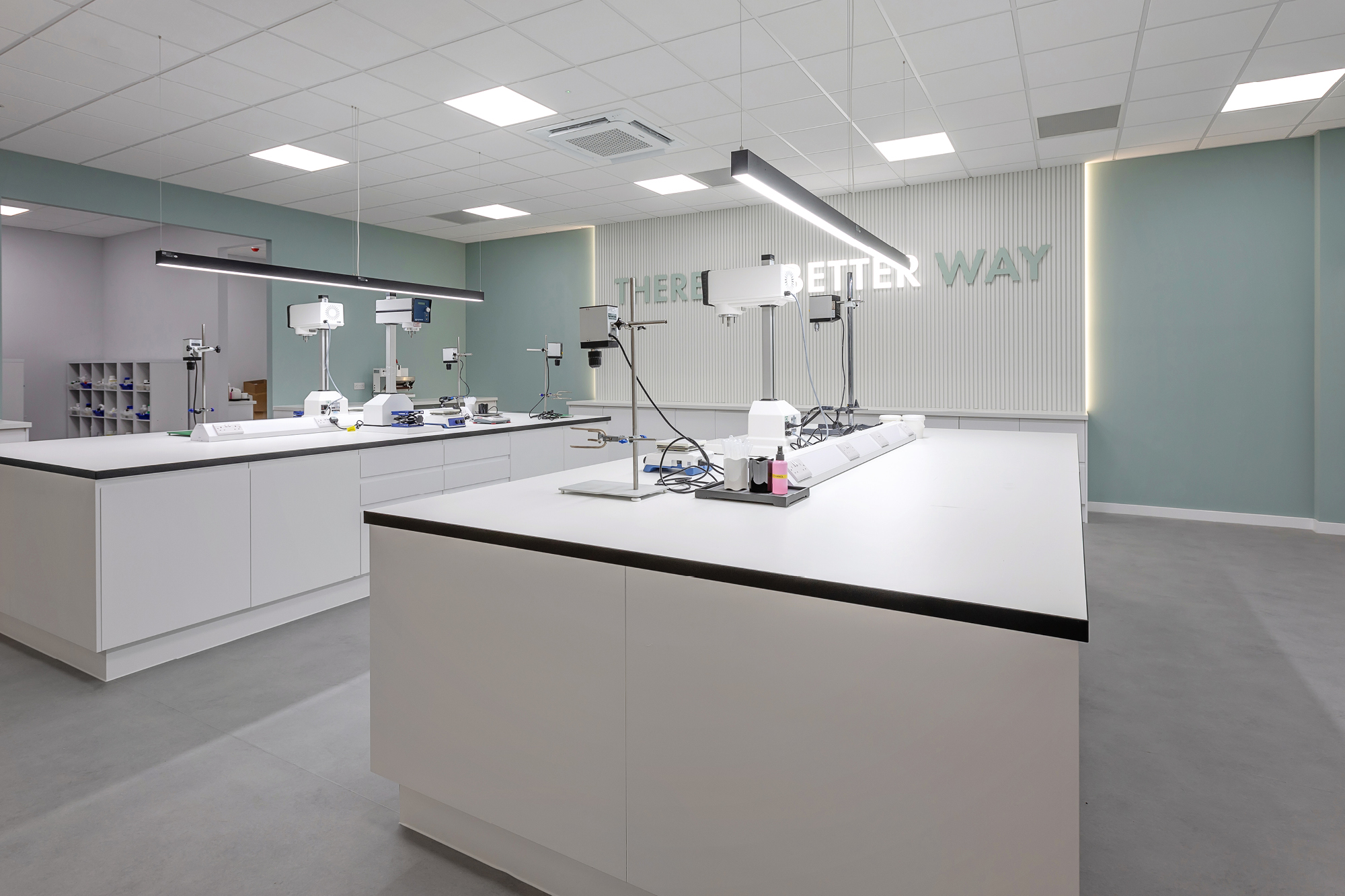 Laboratory space with the word "WAY" on the wall white desking with fawcett and sea green walls.