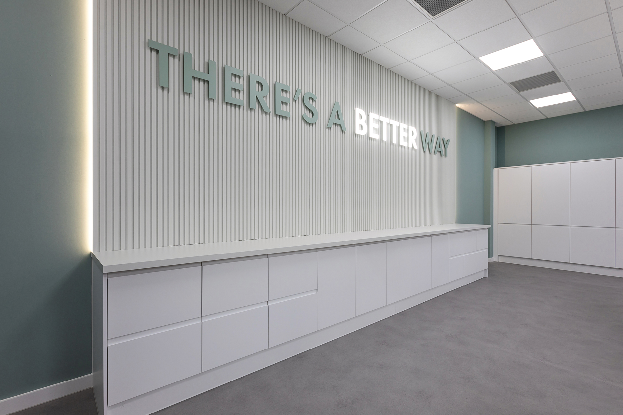 "THERE'S A BETTER WAY" illuminate on wall with white desking and textured back panels.