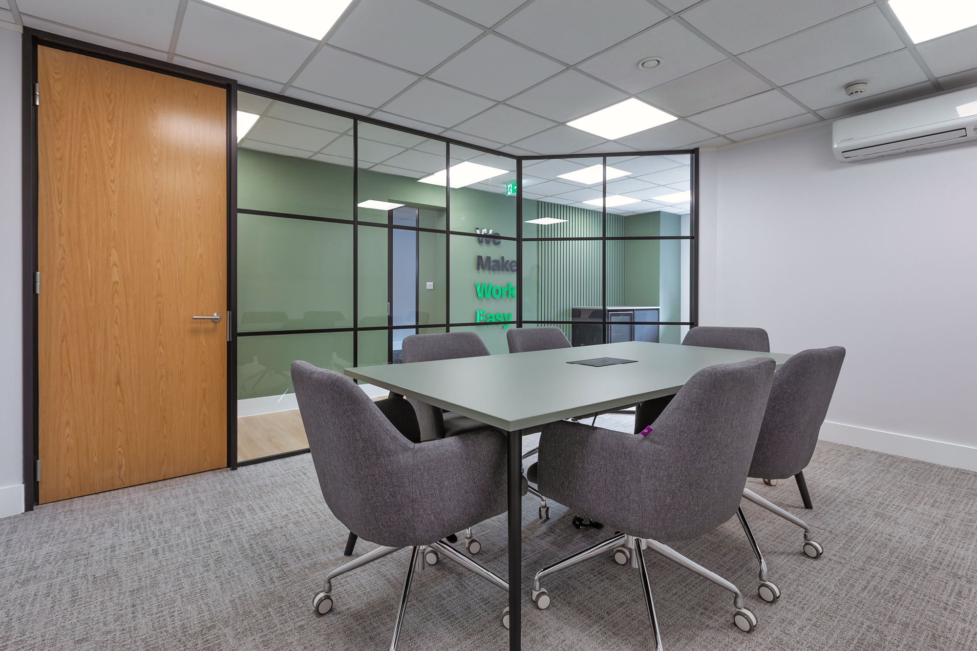 Modern executive boardroom with six grey chairs and an oak door.