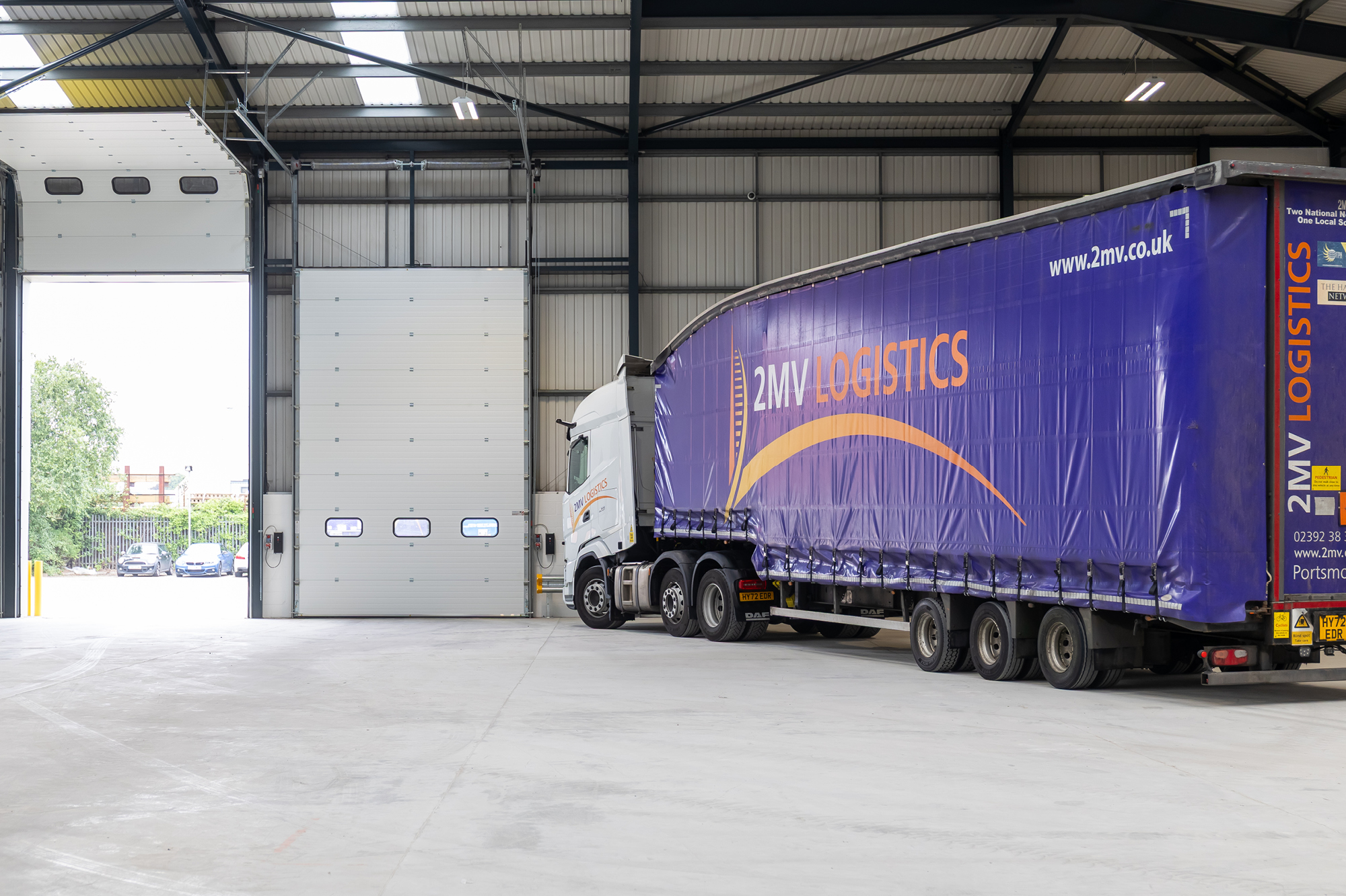 open warehouse with truck inside, logo saying 2MV Logistics