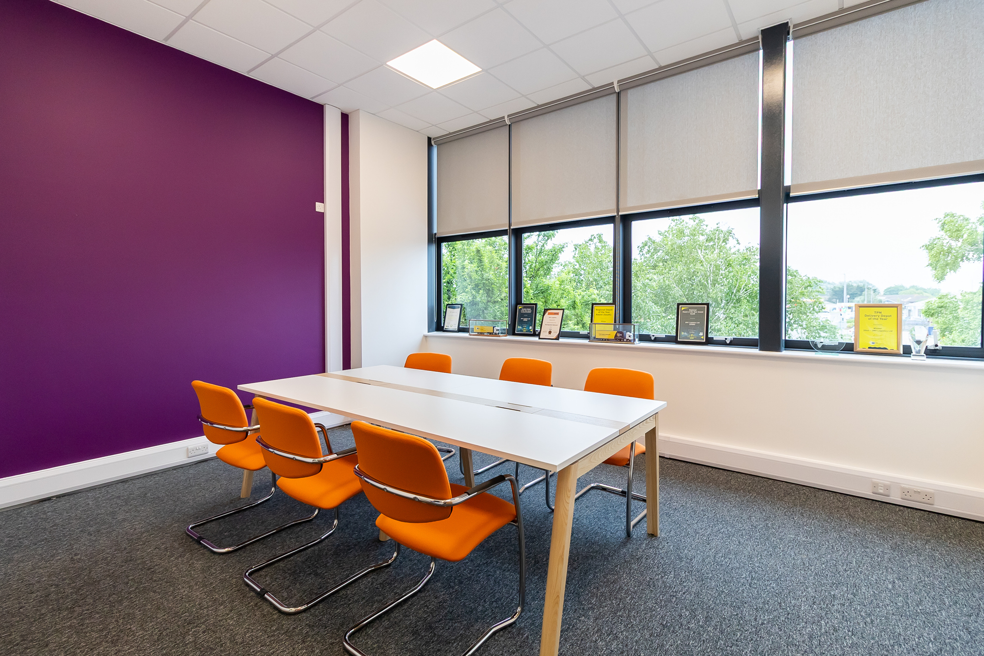 table with ergonomic orange chairs and purple wall with windows