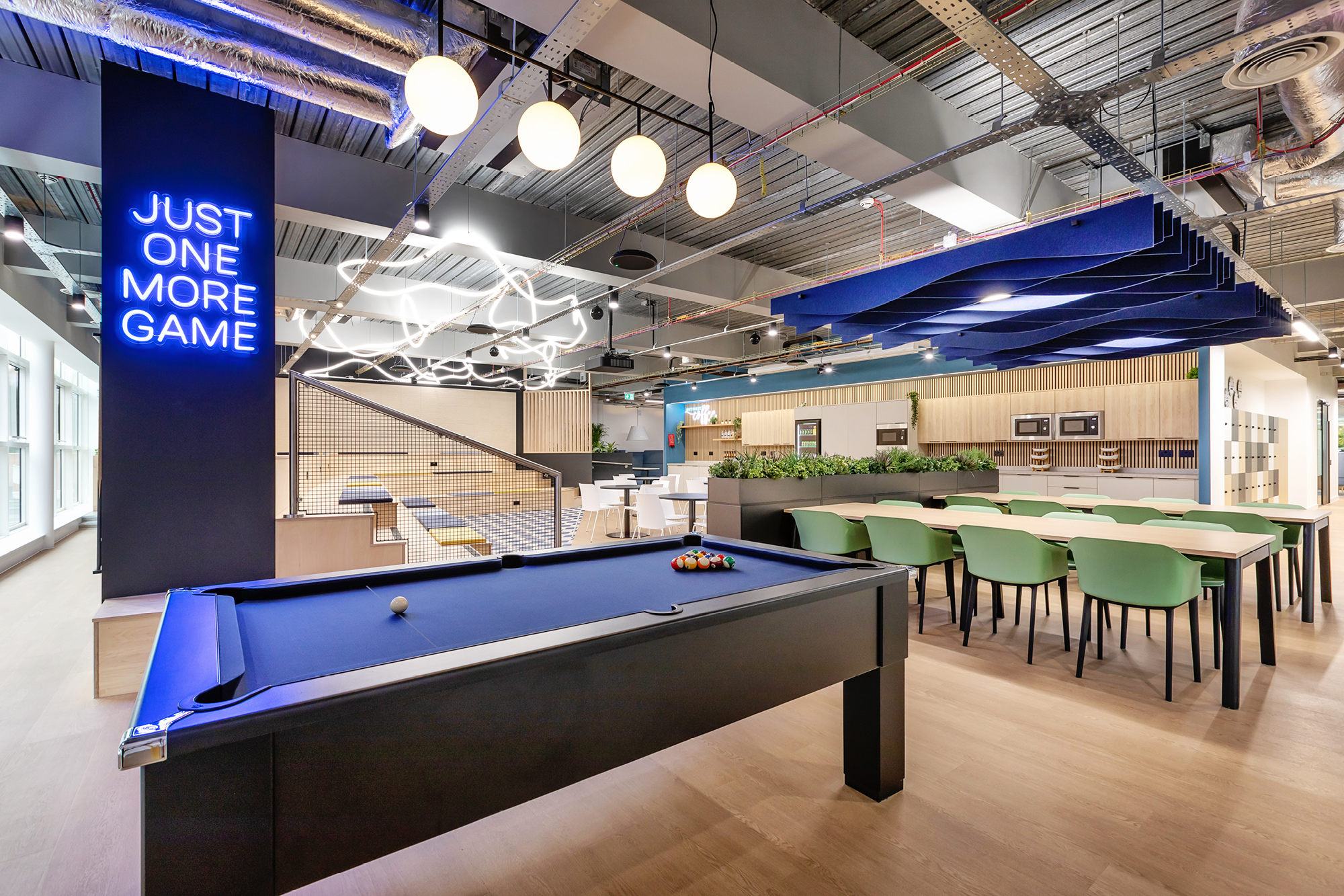 Modern office space with a black pool table in the foreground. Neon sign reads Just One More Game.