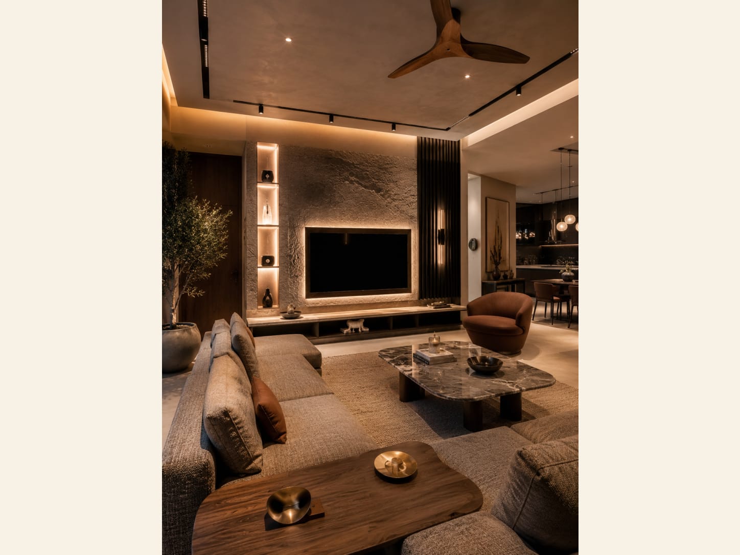 A Modern Living Room with a Stone TV Feature Wall A warm modern living room with a textured stone TV feature wall, backlit niches, a large fabric sectional, a marble coffee table, a rust accent chair, an olive tree and an open-plan dining and kitchen beyond.