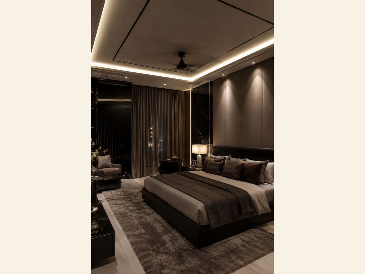 A hushed, hotel-style master bedroom in taupe and espresso, with an upholstered padded wall, a low black platform bed and layered brown bedding.