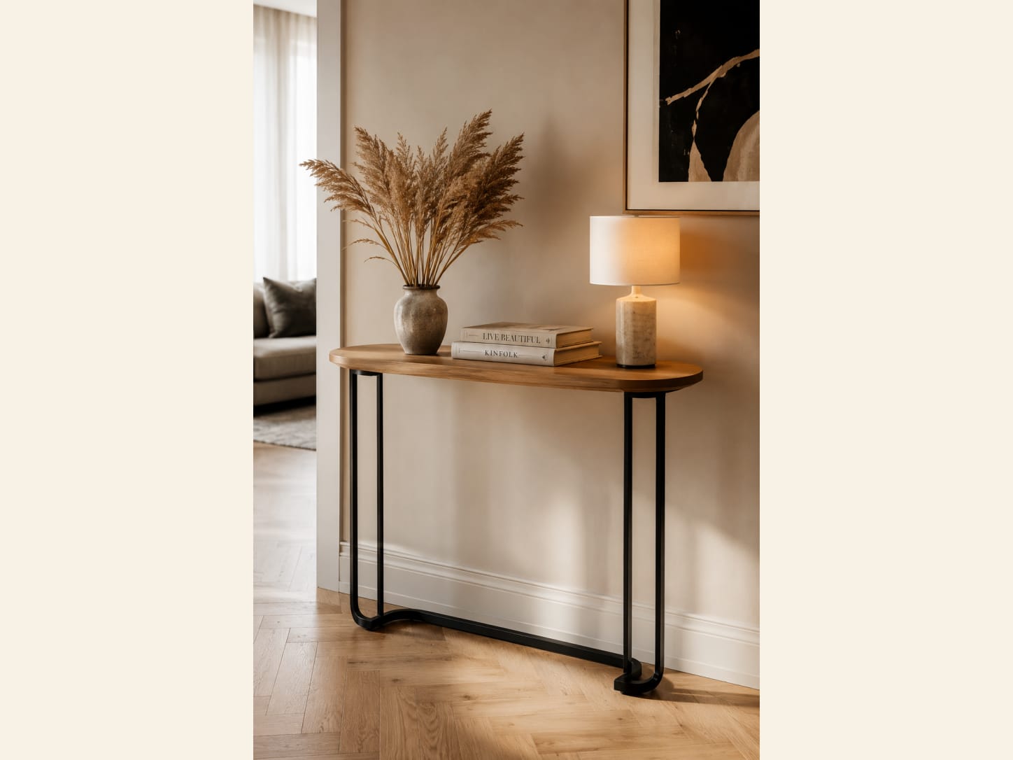 A Curved Oak Console with Black Loop Legs A cosy entryway with a rounded oak console on curved black loop legs, a stone vase of pampas grass, a textured lamp, books and a warm herringbone wood floor.