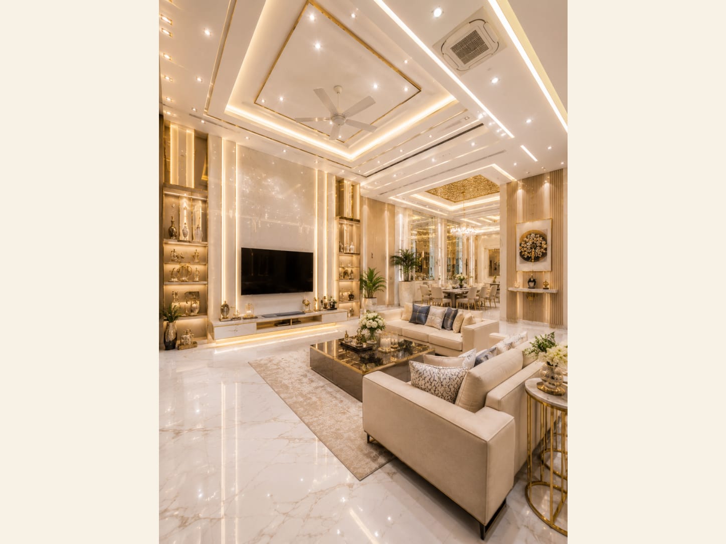 A Gold-Accented Glam Living and Dining Room An opulent open-plan gold-glam living and dining room with fluted columns, twin chandeliers, backlit display walls, and a calm cream-and-marble base.