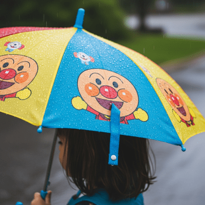 A realistic image of a Children's Umbrella (umbrellas) being used outdoors during a light rain, with droplets visible on the umbrella surface