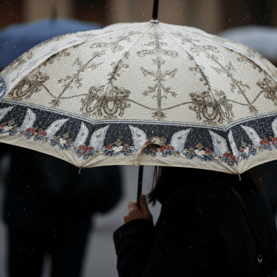 A realistic image of a Fashion Umbrella (umbrellas) being used outdoors during a light rain, with droplets visible on the umbrella surface