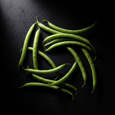 Editorial-style photograph of Green Bean, part of the taxonomy beans, arranged aesthetically on a dark background with dramatic lighting to highlight its shape and color.