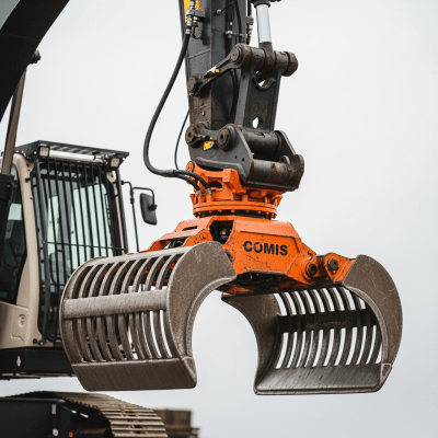 A close-up photograph focusing on the bucket and arm of a Hydraulic material handler (rotating upper, grapple) (excavators), showing details such as hydraulic lines, metal textures, and wear marks