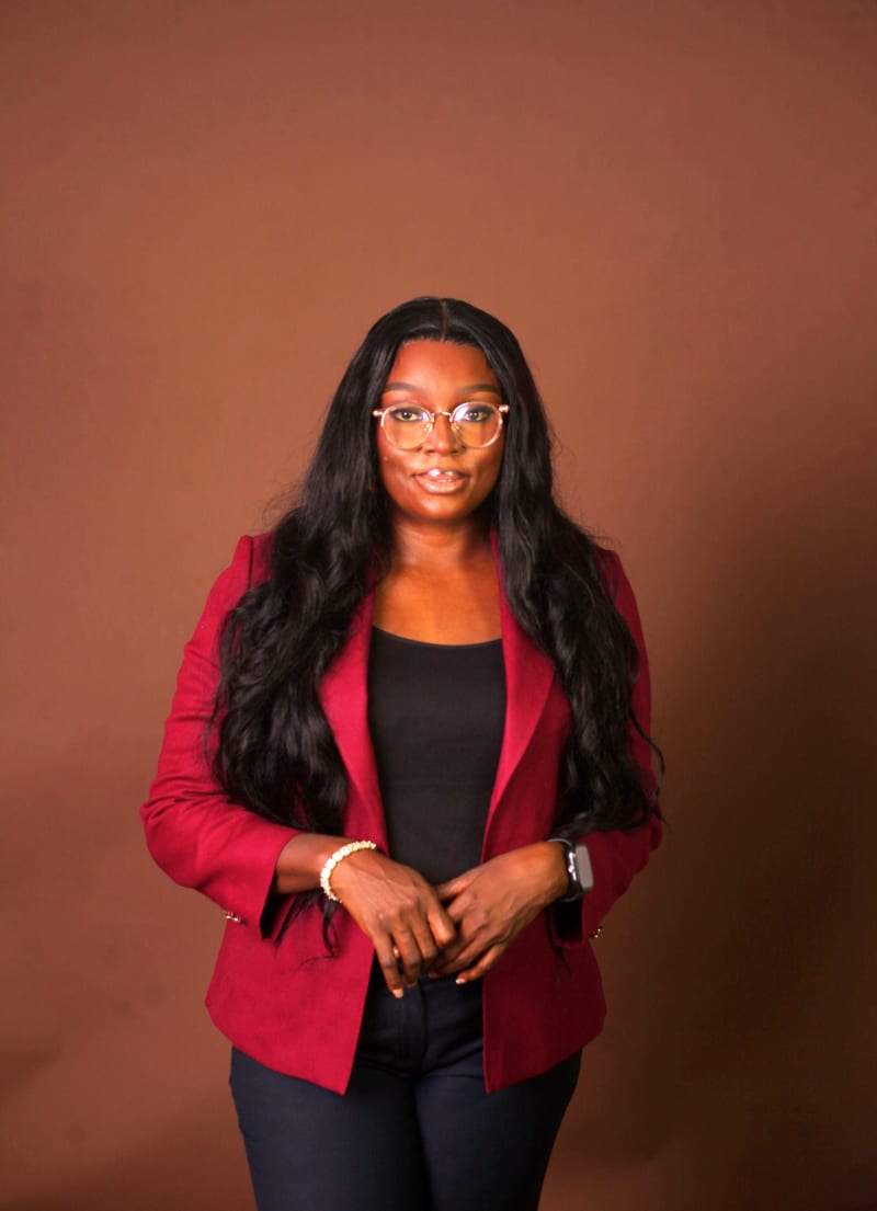 Mfoniso Nyong, founder of Bellanath Strategy, in a red blazer against a warm brown backdrop.
