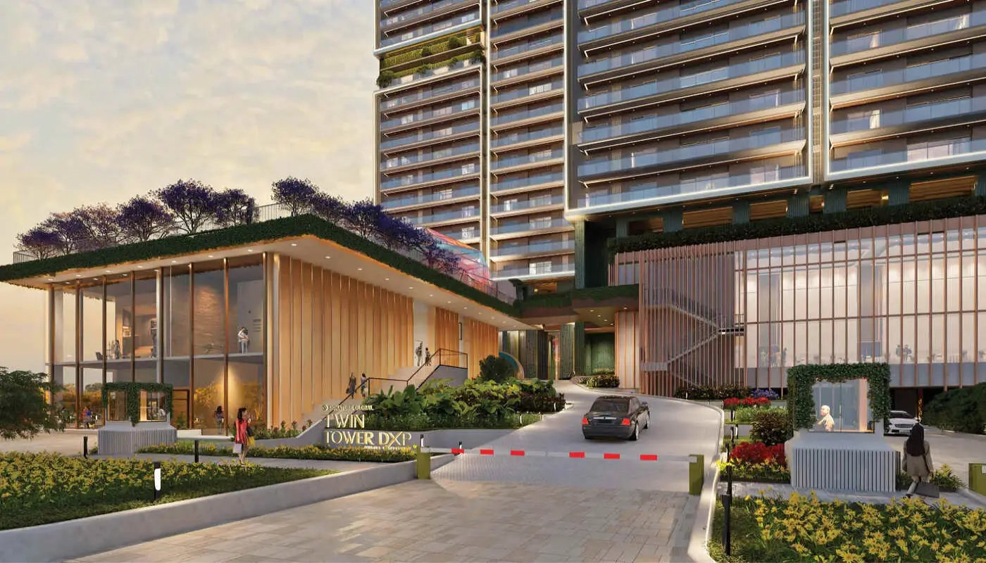 Modern building entrance with landscaped gardens and a driveway leading to the main structure.