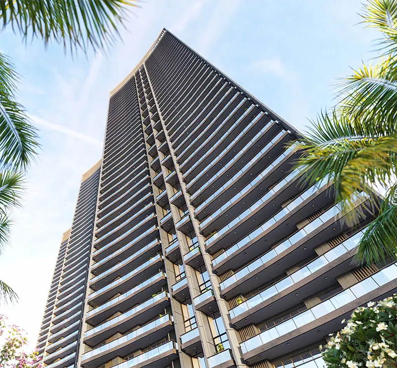 Tall residential building with balconies, surrounded by palm trees and a clear sky.